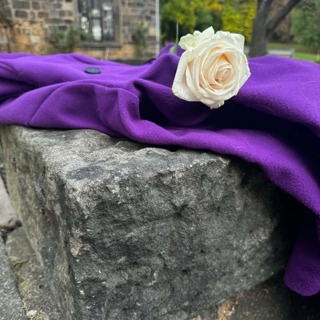 A white rose resting on Helena’s purple coat, laid over an old Yorkshire stone wall